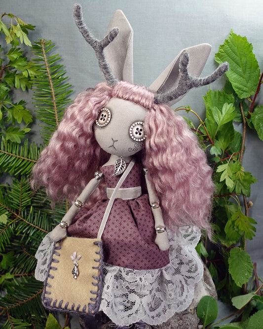 a jackalope girl art doll with button eyes, antlers and rabbit ears in a dusky rose dress