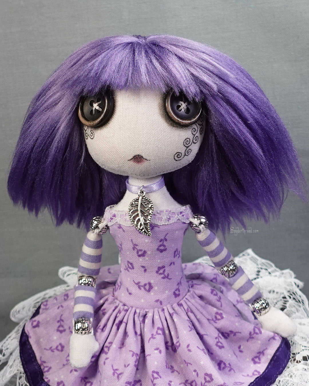 a button eyed cloth art doll with purple hair and dress