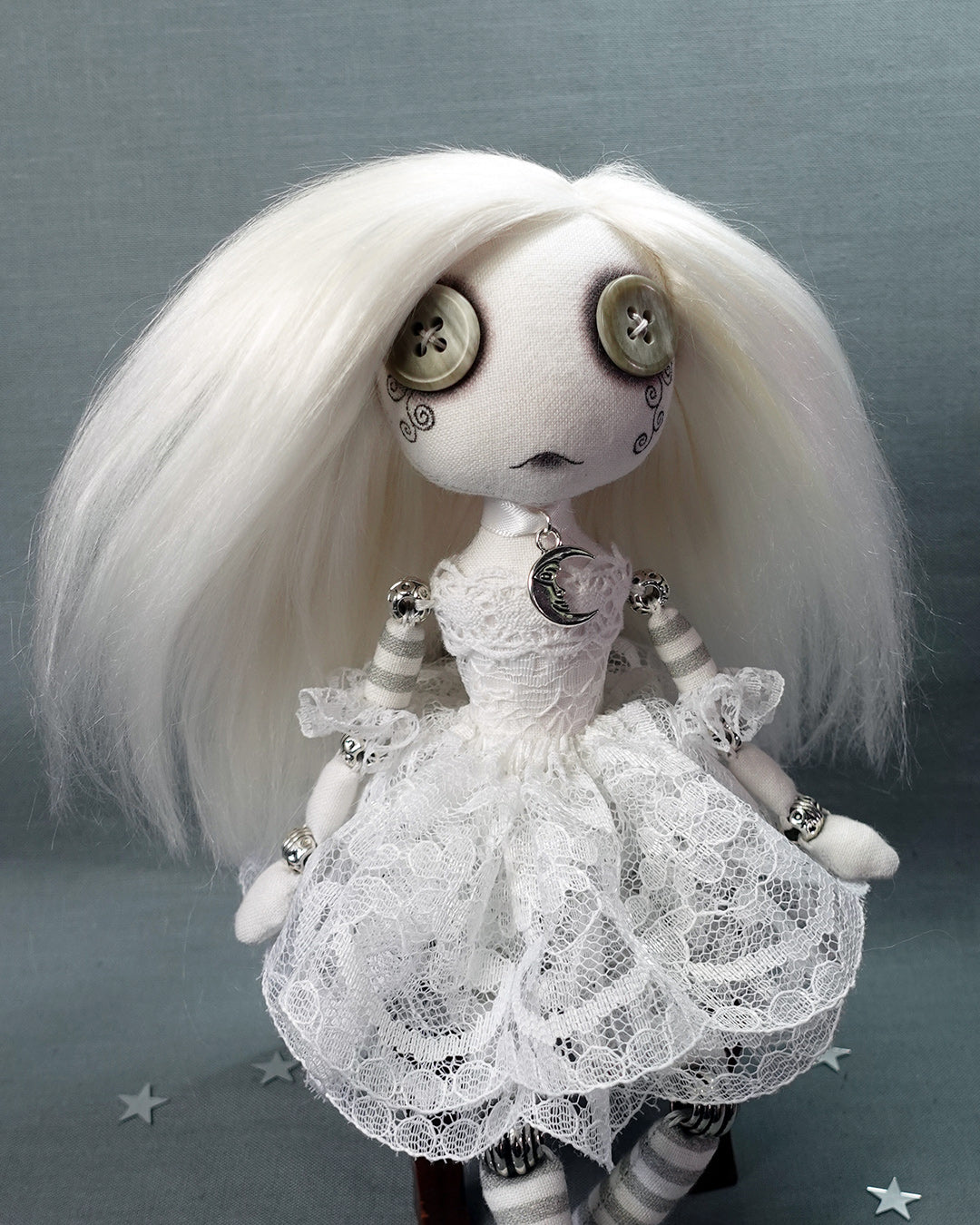 a white cloth ghost doll with grey button eyes, moon necklace and white lace dress