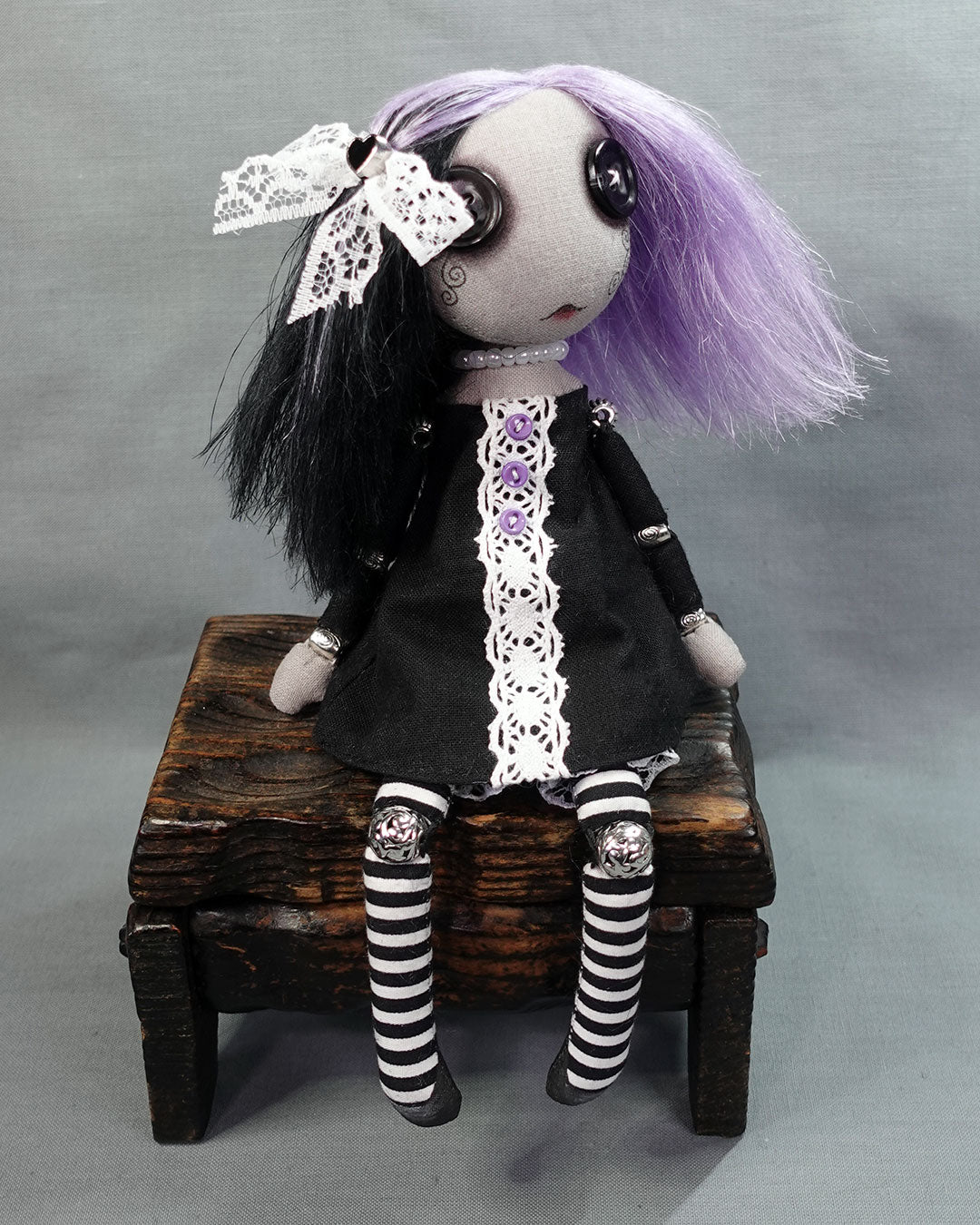 a button eyed goth doll in black and white dress with purple and black hair and white lace hair bow