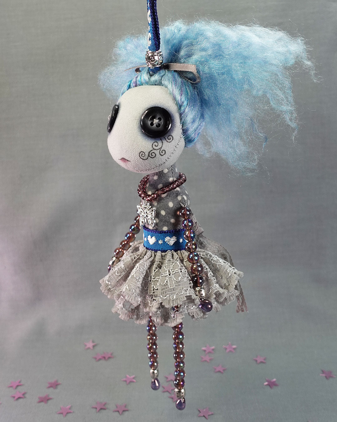 a hanging button eyed art doll with blue hair and purple glass beaded limbs
