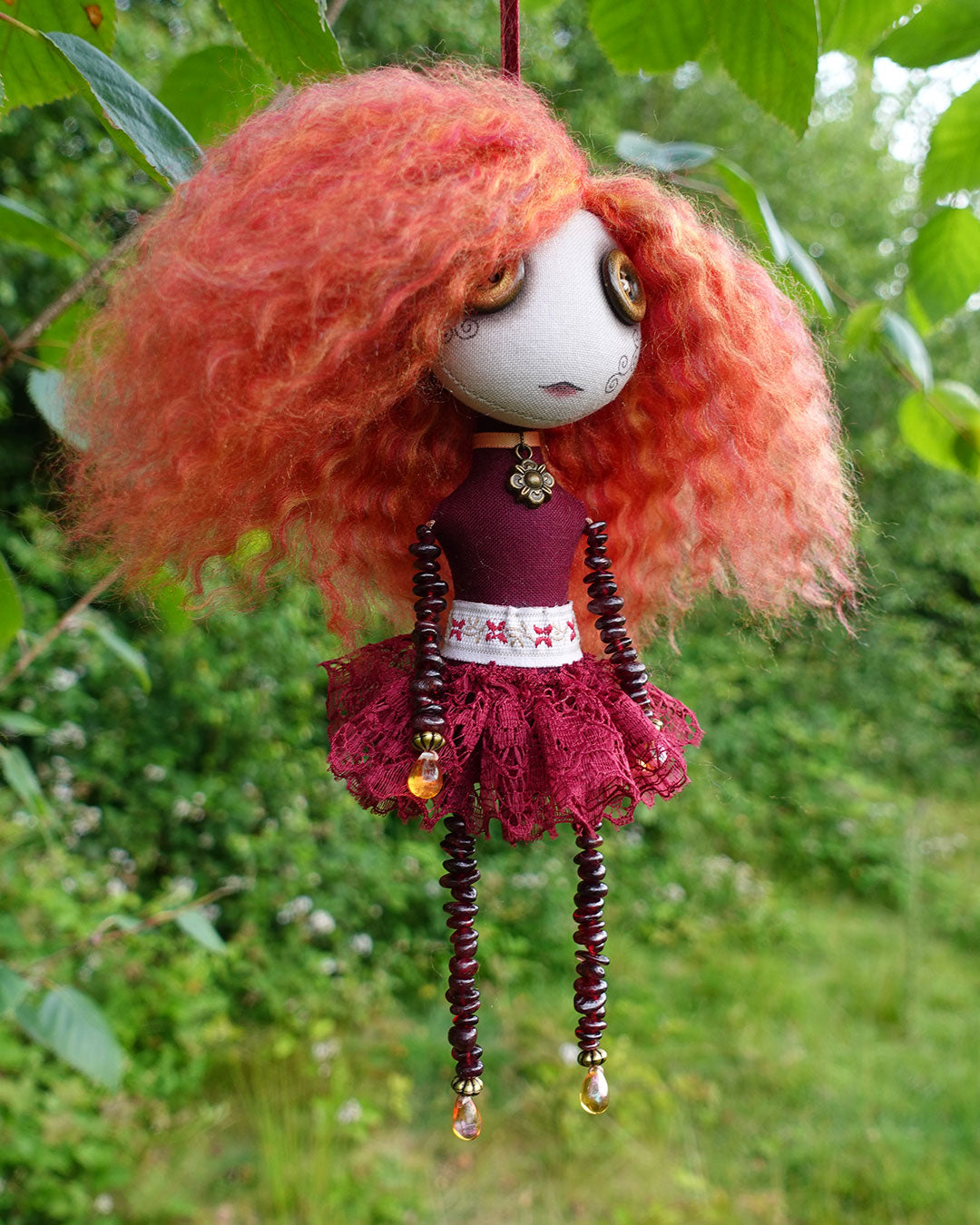a hanging cloth art doll in reds and golds with garnet stone beaded limbs