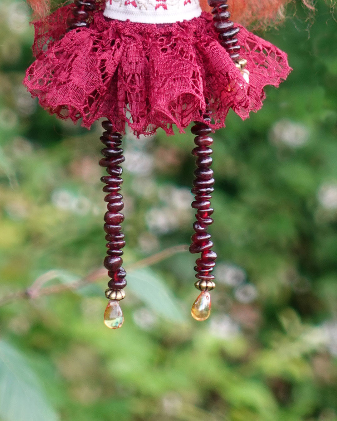 a hanging cloth art doll in reds and golds with garnet stone beaded limbs