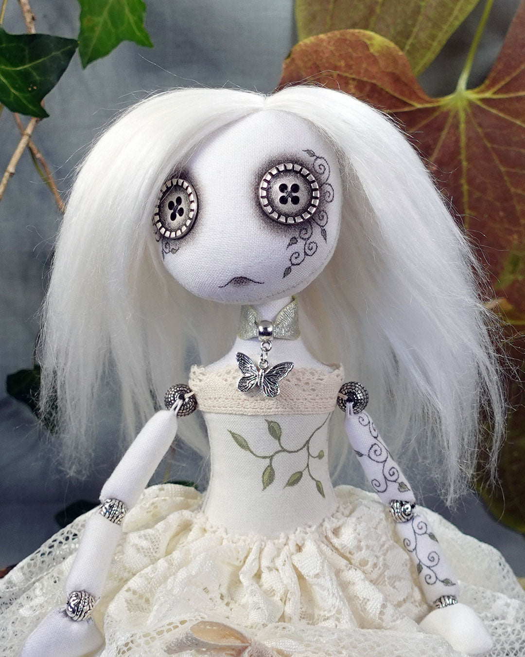 Button eyed art doll with white hair and detailed face, wearing a white dress with lace details.