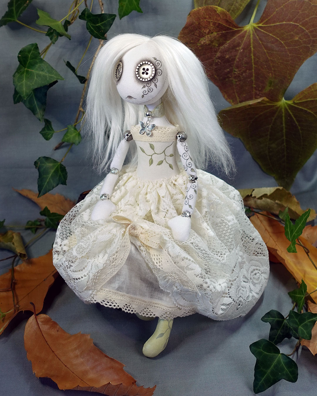 Pale ghost art doll with white hair and lace dress surrounded by autumn leaves