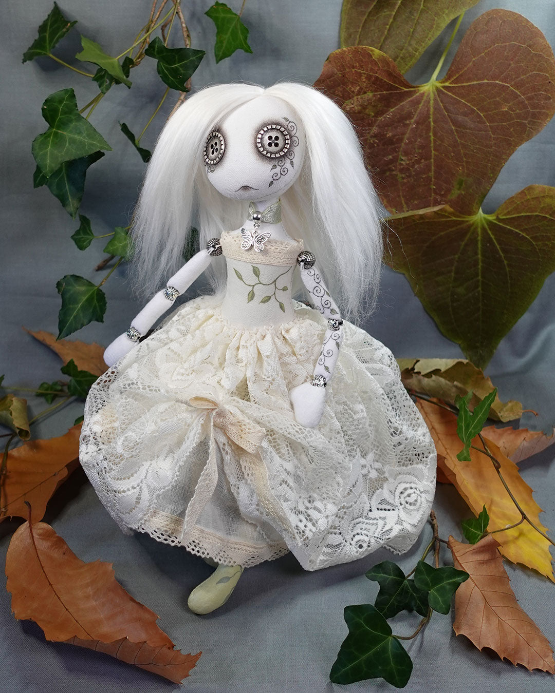 Button eyed gothic ghost doll with white hair and lace dress surrounded by autumn leaves