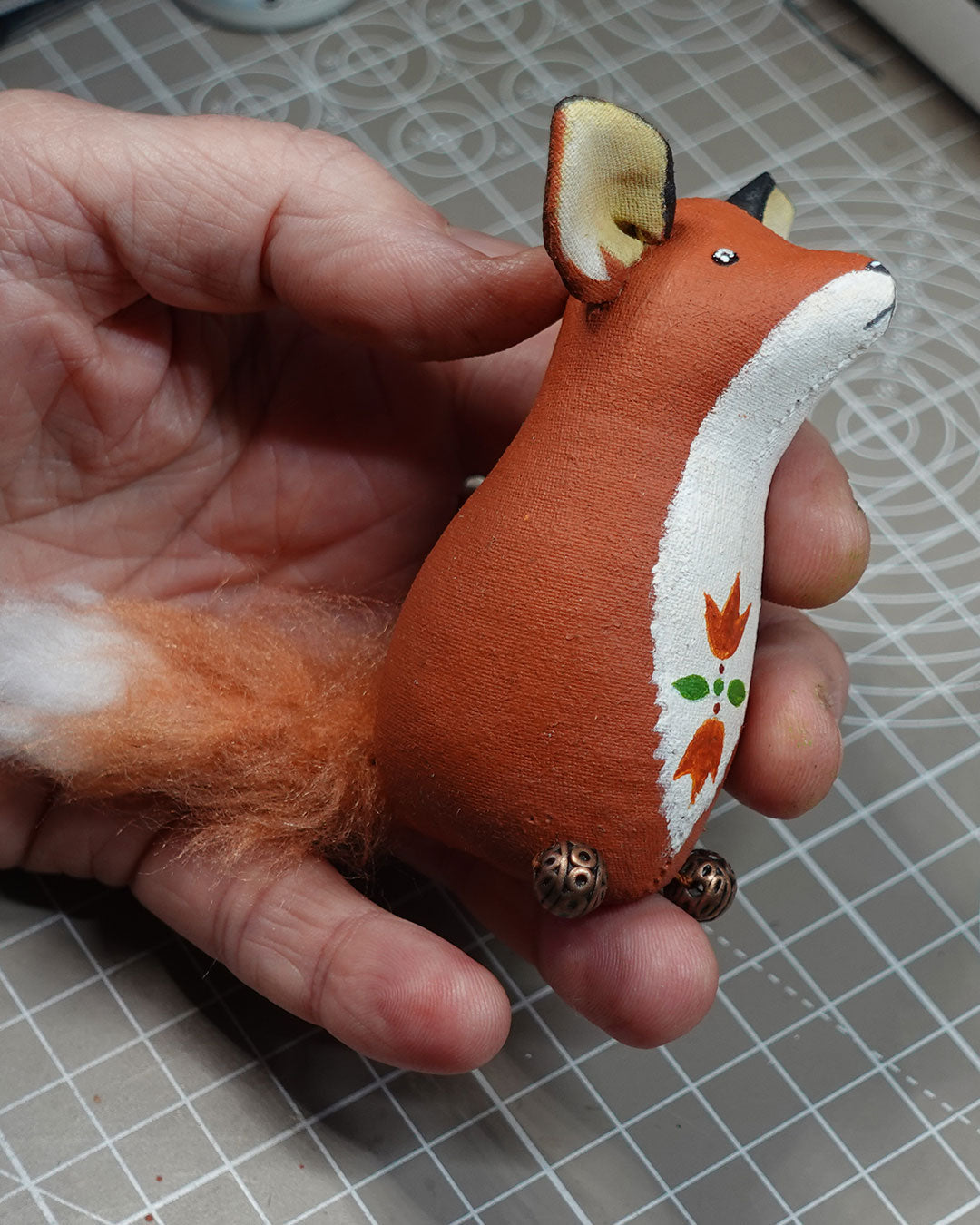 Hand holding a small fox figurine on a grid surface