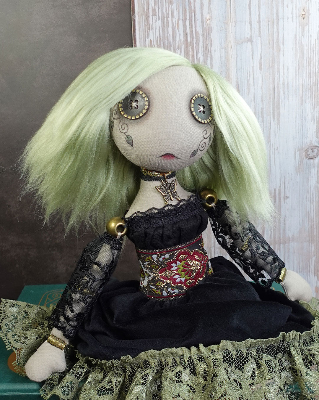 Art doll with green hair and butterfly necklace on a textured surface