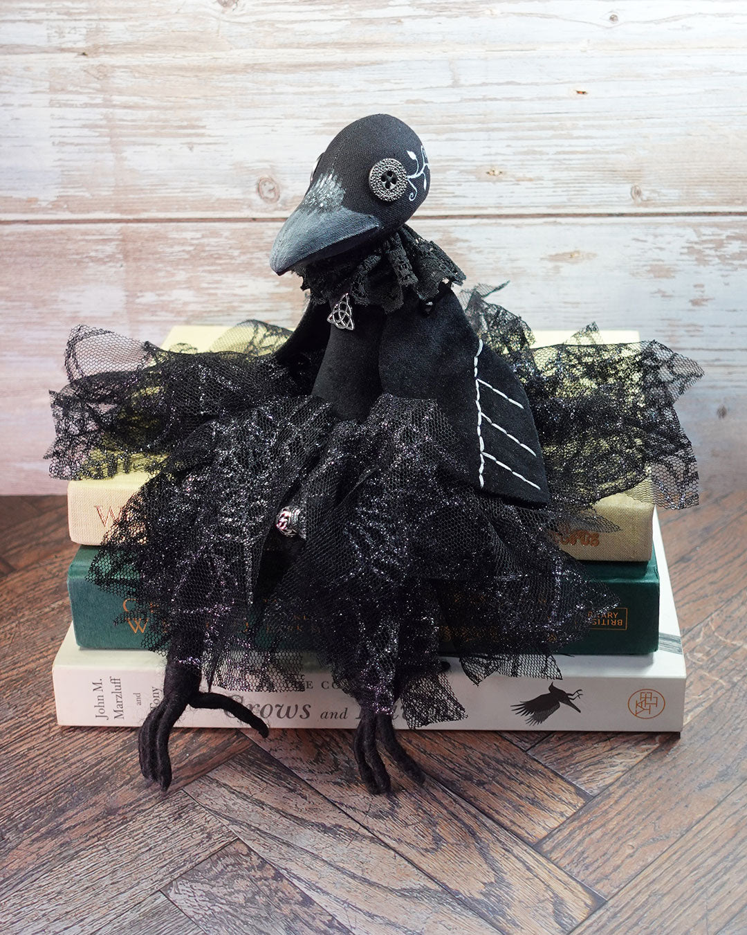 gothic crow art doll sitting on a pile of books