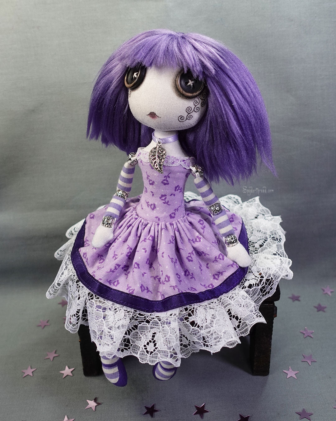 a button eyed cloth art doll with purple hair and dress