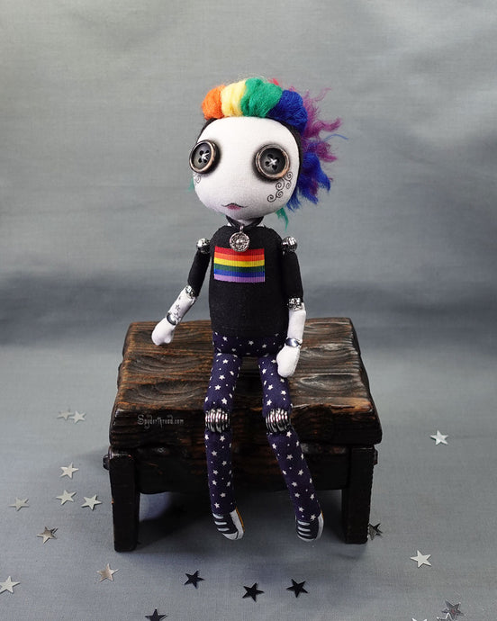 A button eyed cloth art doll with rainbow hair, in pride flag t-shirt and star print jeans