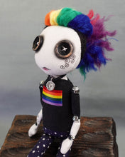 Close up of cloth art doll with button eyes and rainbow hair wearing pride flag t-shirt