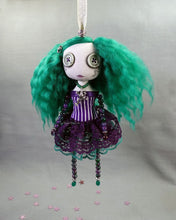 a hanging beaded cloth art doll with button eyes and green hair, in green and purple dress