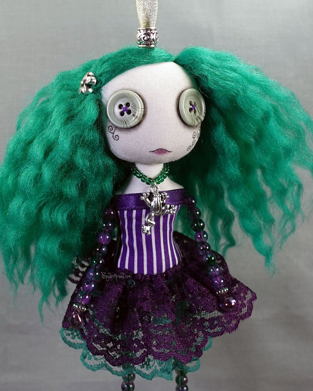a hanging beaded cloth art doll with green hair in green and purple dress
