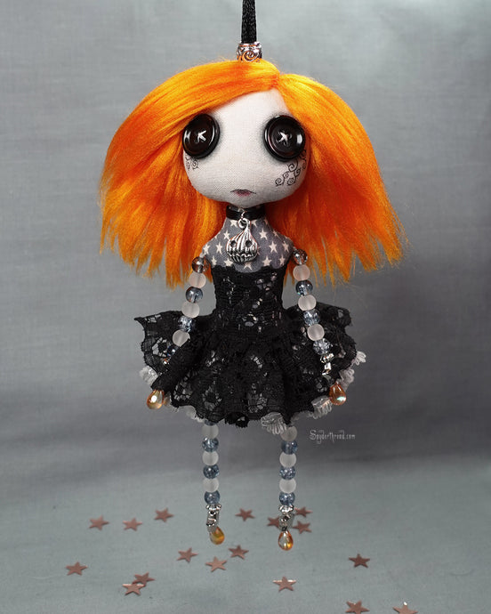 a hanging cloth doll with bright orange hair in black and grey lace with pumpkin necklace