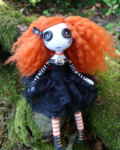 a Gothic cloth doll with button eyes and orange hair, in black dress with halloween pumpkin charm