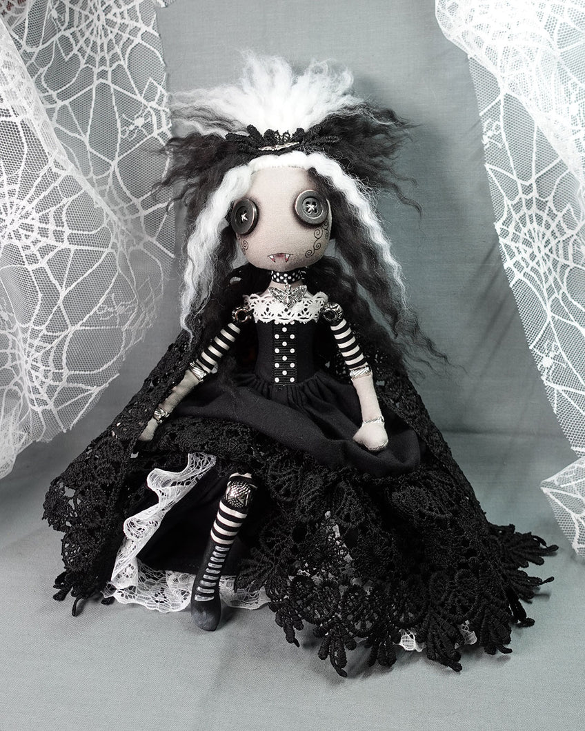 a cloth vampire art doll with button eyes in long black and white dress