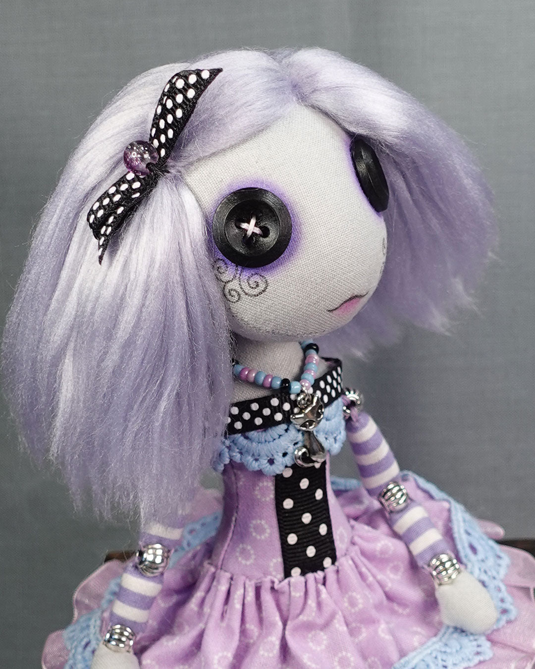 close up of button eyed doll with pastel lavender hair and polka dot bow
