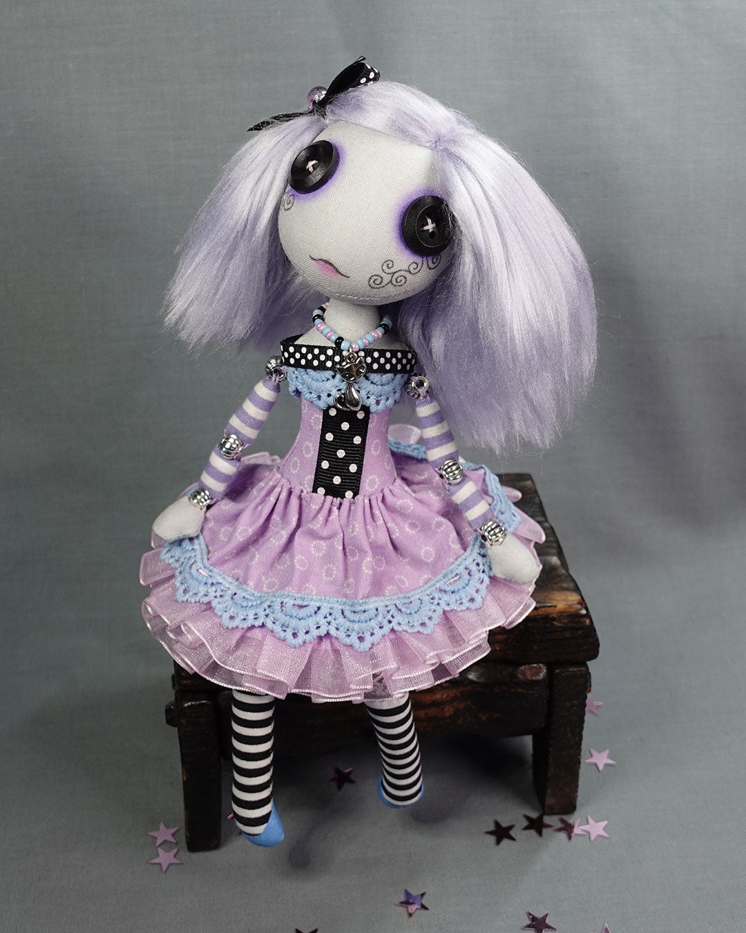 a cloth art doll with button eyes dressed in pastels with black and white polka dot trim