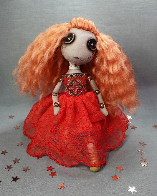 a cloth art doll with button eyes, rose gold hair and red dress