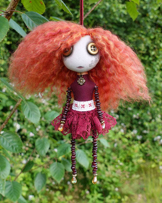 a hanging cloth art doll in reds and golds with garnet stone beaded limbs
