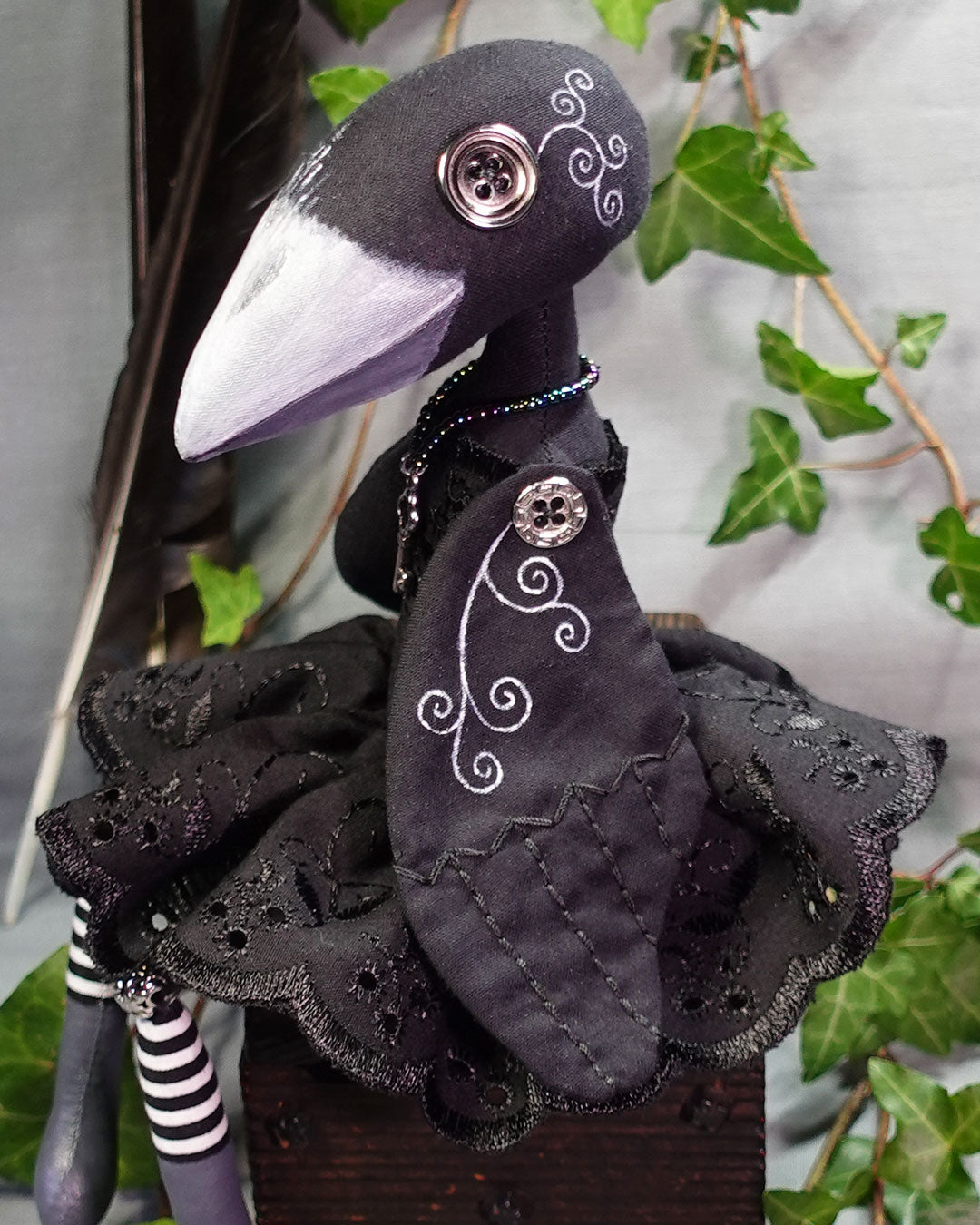 close up of black crow art doll with white hand painted line detail and embroidery