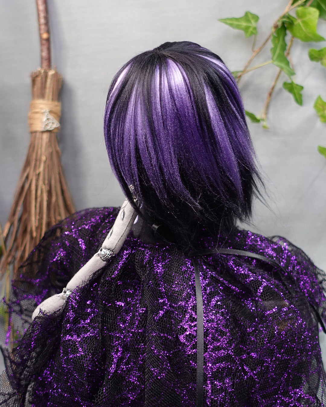 art doll with purple and black hair wearing a purple outfit with a broom in the background