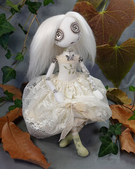 Textile art doll with white hair and detailed clothing among leaves
