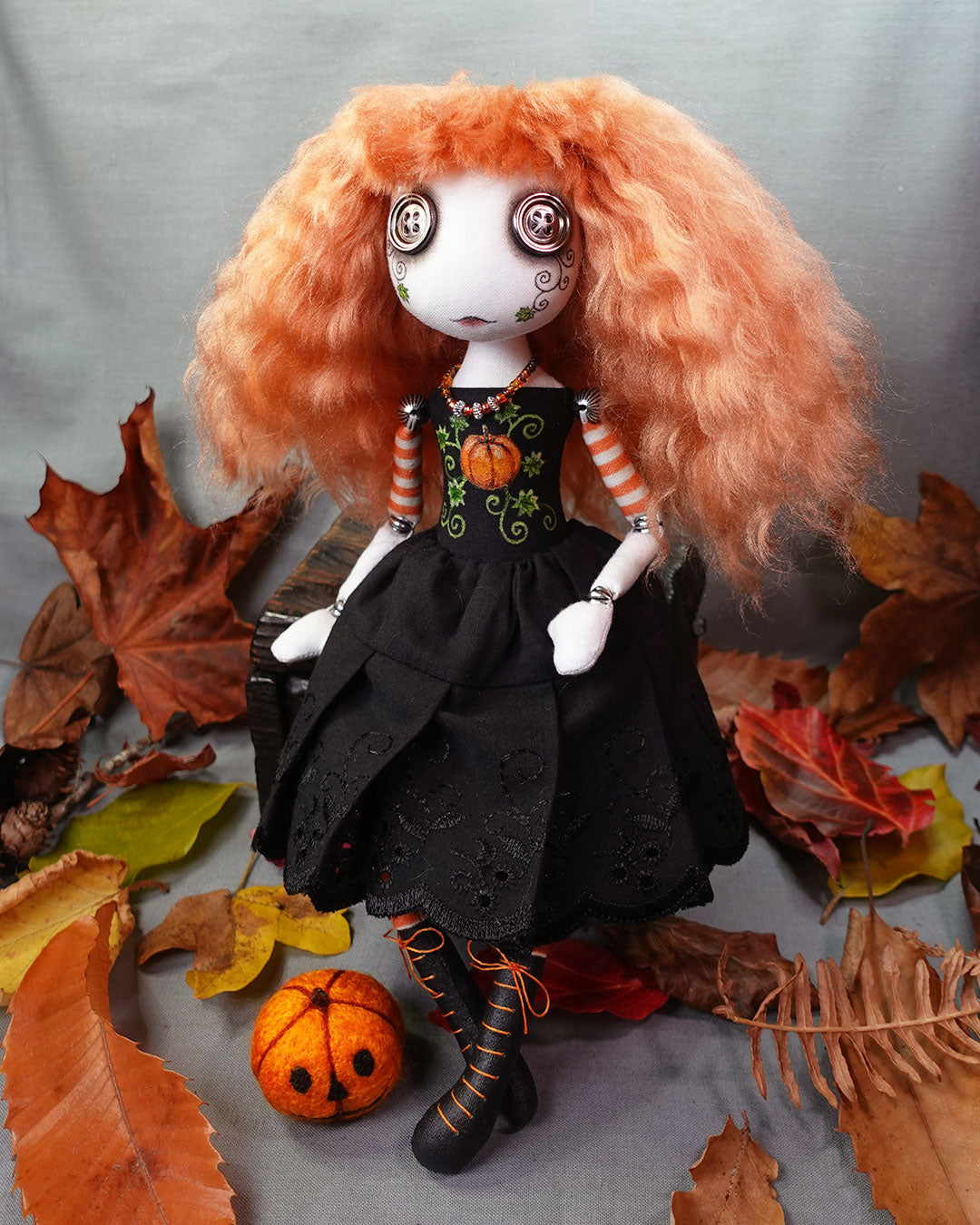 Doll with orange hair and black outfit with pumpkin design surrounded by autumn leaves