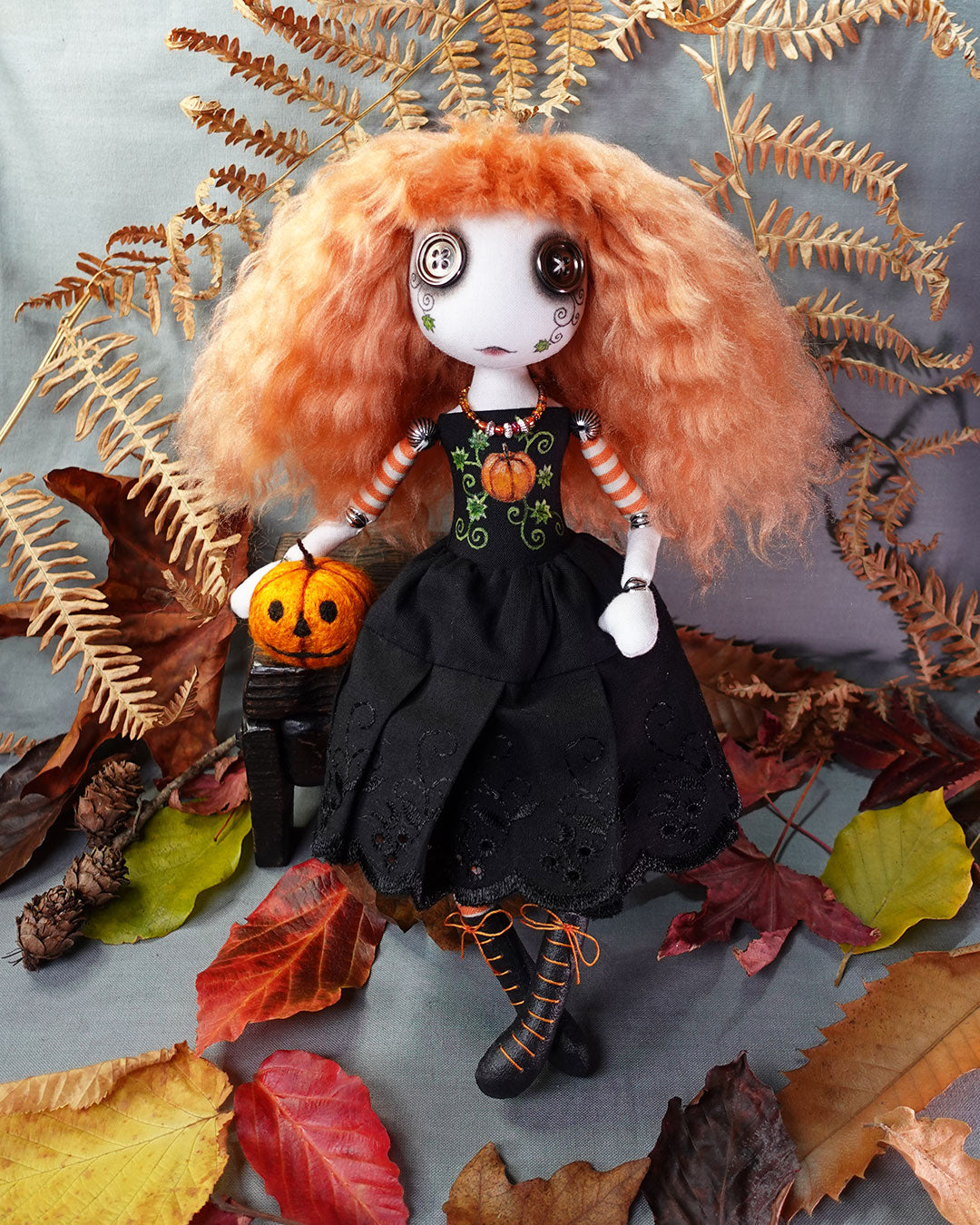 Doll with orange hair and black dress surrounded by autumn leaves and pumpkin