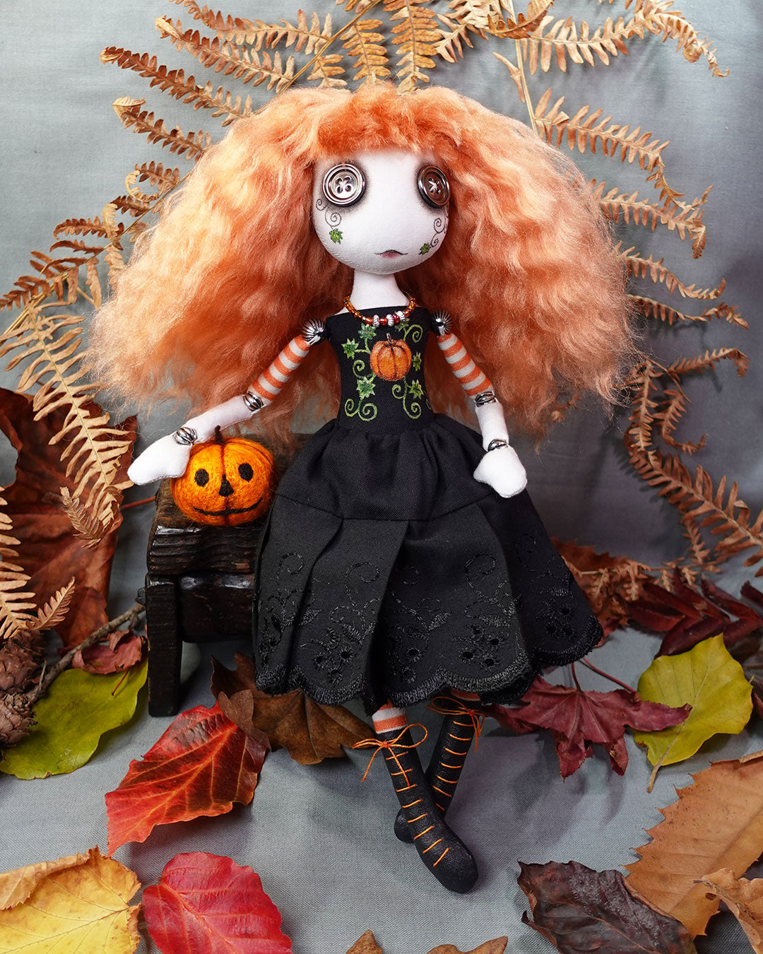 Doll with orange hair and black dress surrounded by autumn leaves and a small pumpkin