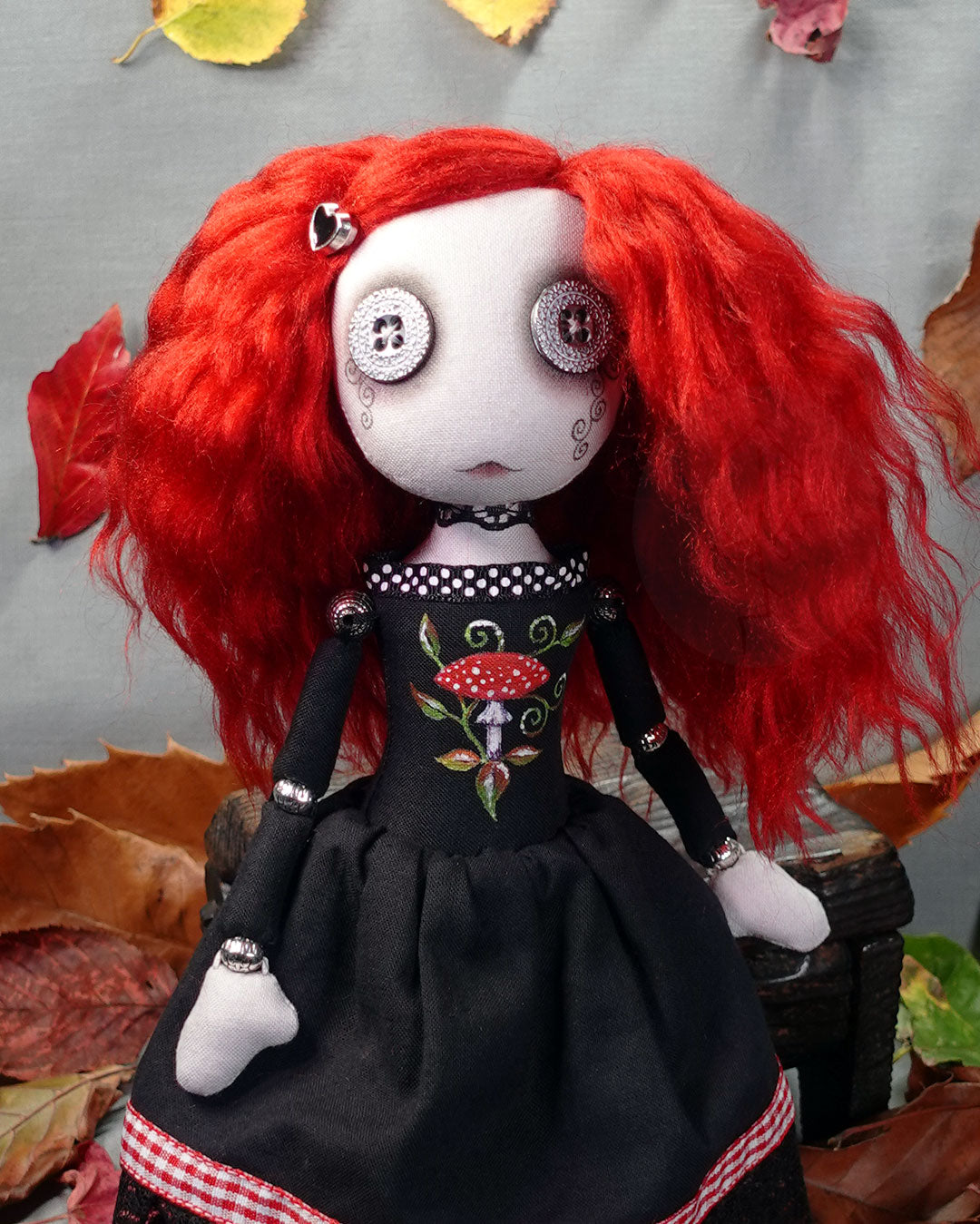 Art doll with red hair and a black dress with mushroom design on a gray background with autumn leaves