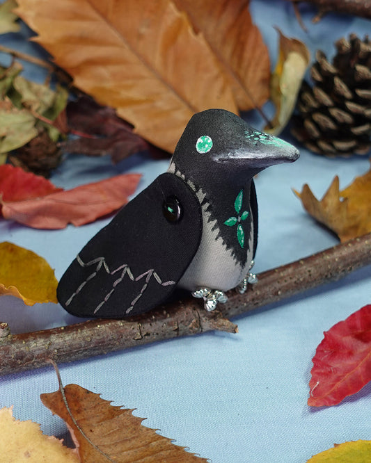 Decorative bird figurine with green eyes and floral design on a branch with autumn leaves and pinecones.