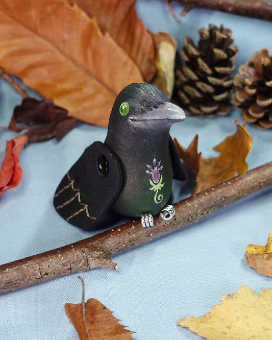 Decorative crow figurine with floral design on a branch with autumn leaves and pinecones
