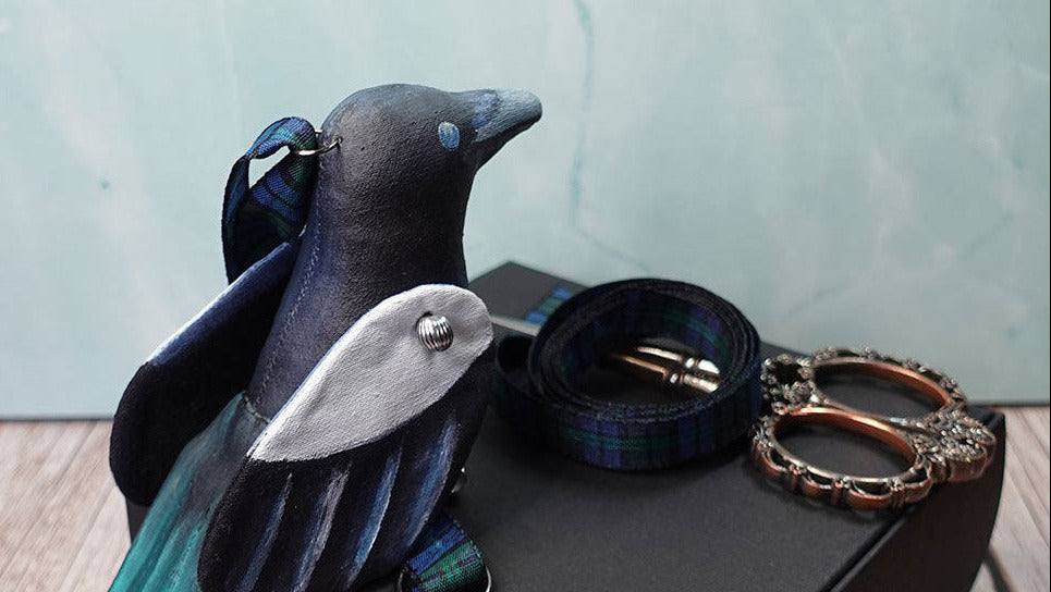 magpie bird ornament sitting on black box with ornate scissors and ribbon