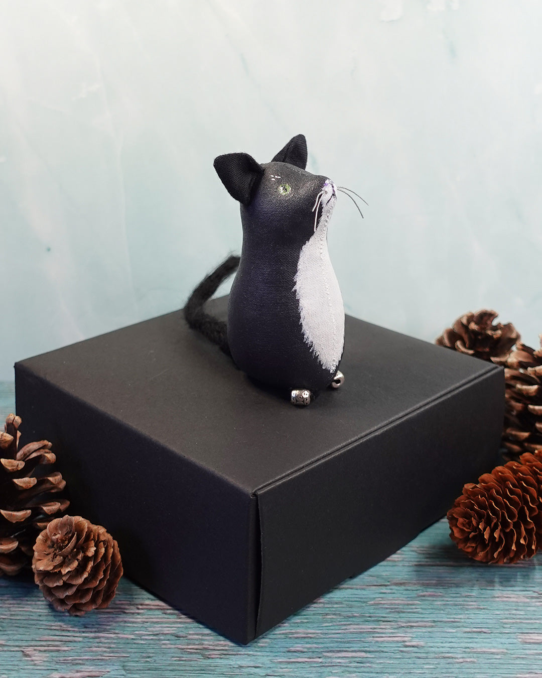 Black and white cat figurine on a black box with pine cones around