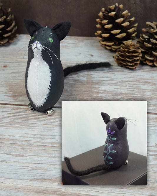 Black and white cat figurine with a close-up inset on a wooden surface with pinecones.