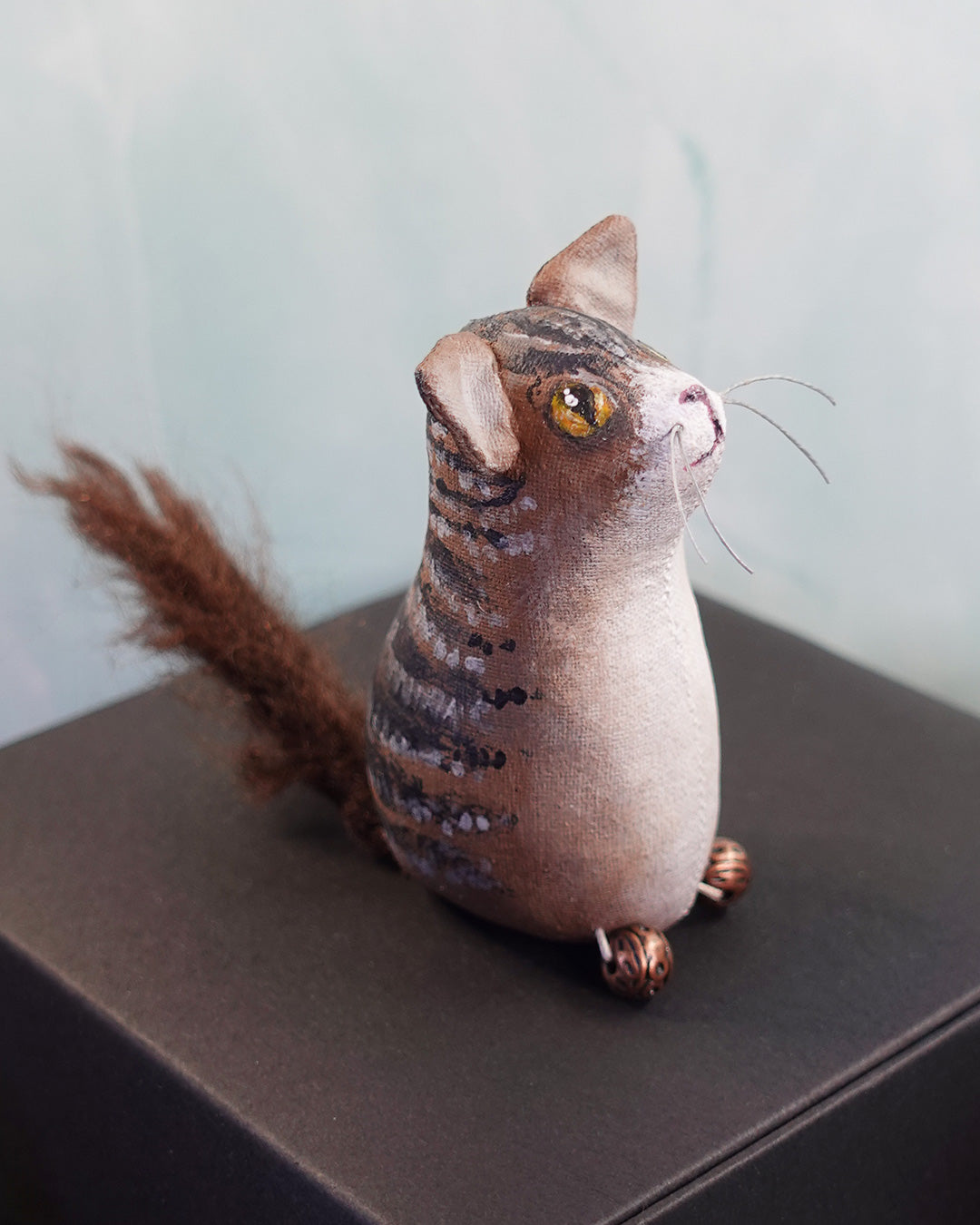 textile tabby cat figure with yellow eyes and bushy tail on a dark surface.