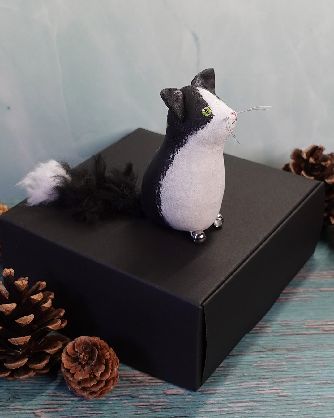 Black and white cat figurine on a black box with pine cones around