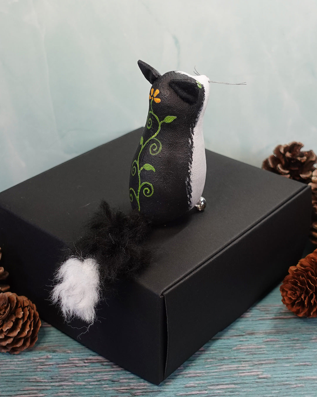 Black and white cat figurine with floral design on a black box against a light blue background.