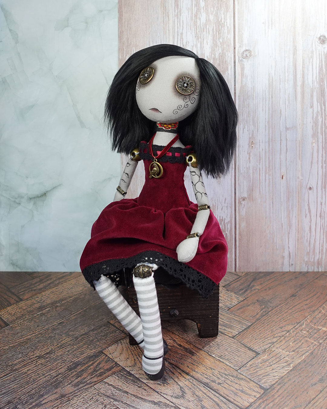 Art doll with button eyes, black hair and red velvet dress sitting on a wooden box.