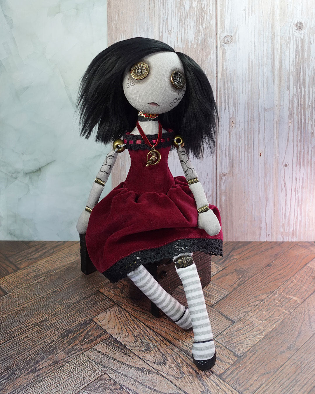 Textile doll with black hair and red velvet dress sitting on a wooden box.
