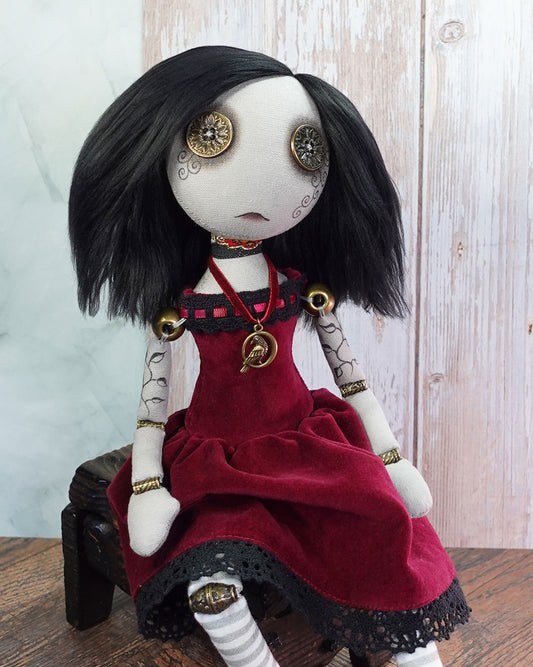 Art doll with black hair and a red dress sitting on a wooden surface.