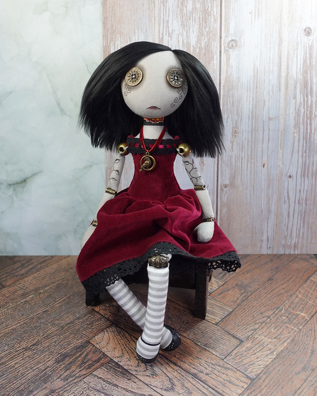 Button eyed art doll with black hair and red dress sitting on a wooden box.