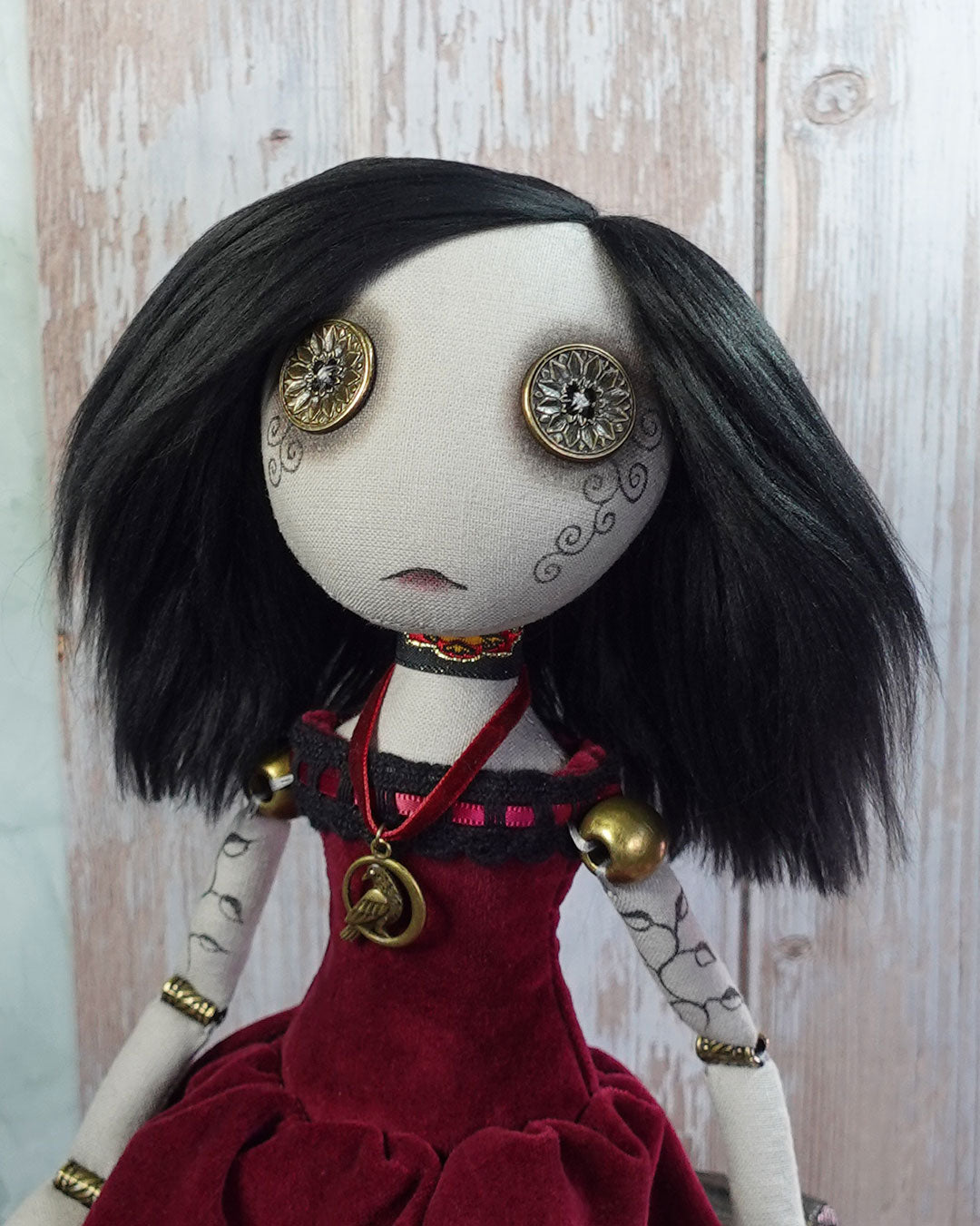 Art doll with black hair, red dress, and decorative bead joints on a wooden background