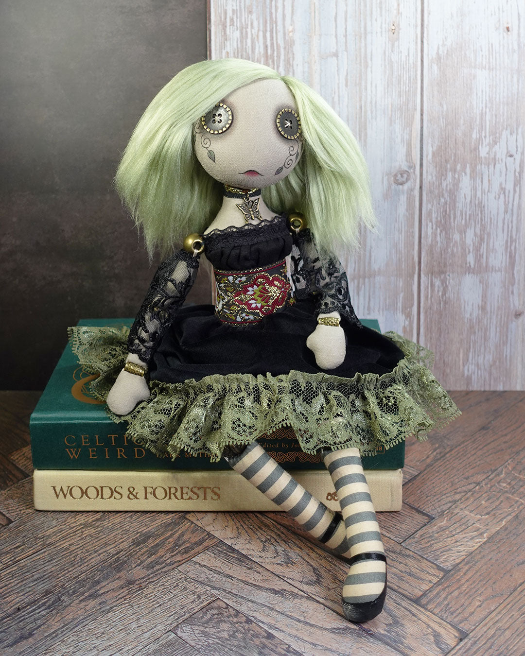 Art doll with green hair and striped legs sitting on a book titled 'Woods & Forests'.