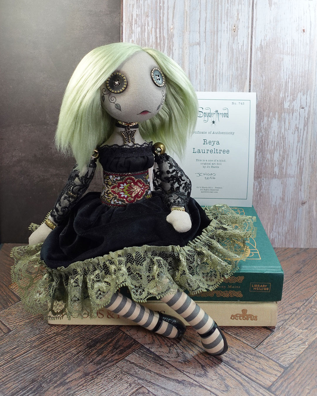 Art doll with green hair and black dress on a wooden surface with books and certificate of authenticity in the background