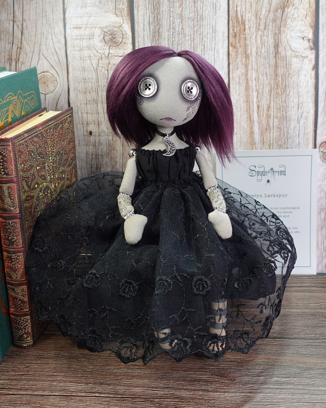 Gothic-style doll with purple hair and black lace dress on a wooden shelf with artist's certificate of authenticity