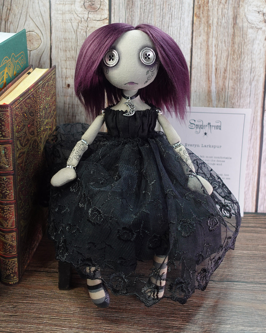 Gothic-style doll with purple hair and black lace dress on a wooden surface