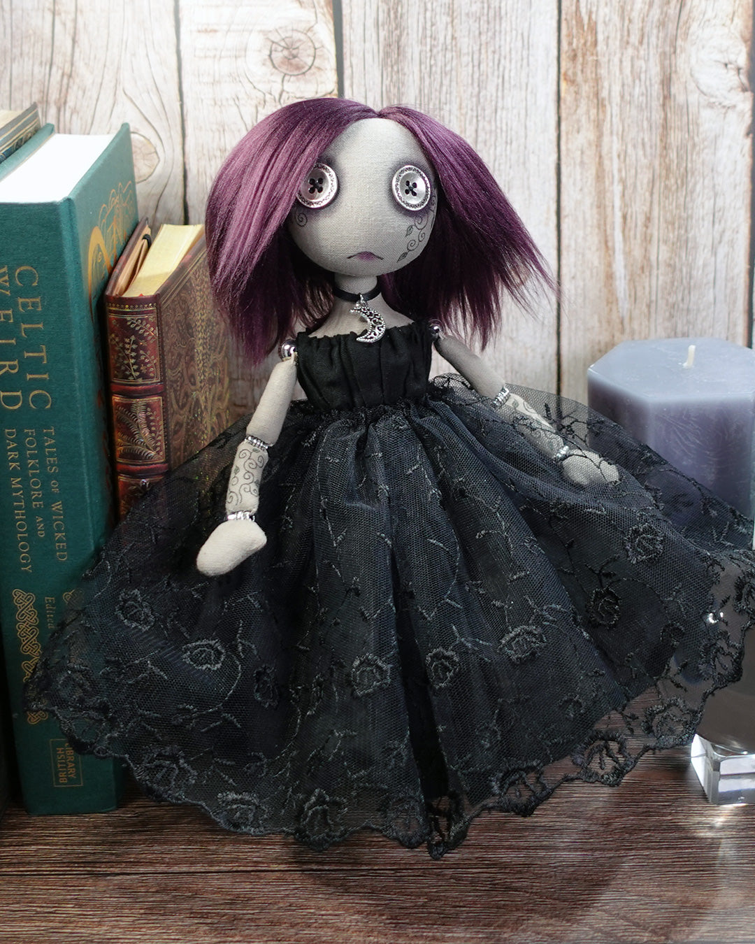 Gothic-style doll with purple hair and black lace dress in front of books and a candle.